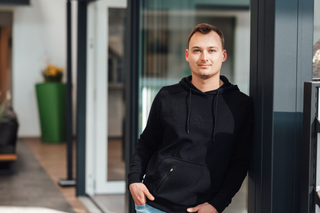 Nick Schütte lehnt mit seiner linken Schulter am Wintergarten und guckt freundlich in die Kamera