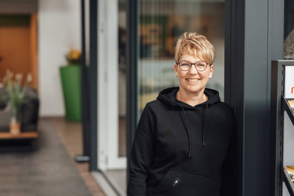 Meike Hippel lehnt mit der linken Schuler am Wintergarten und lächelt freundlich in die Kamera