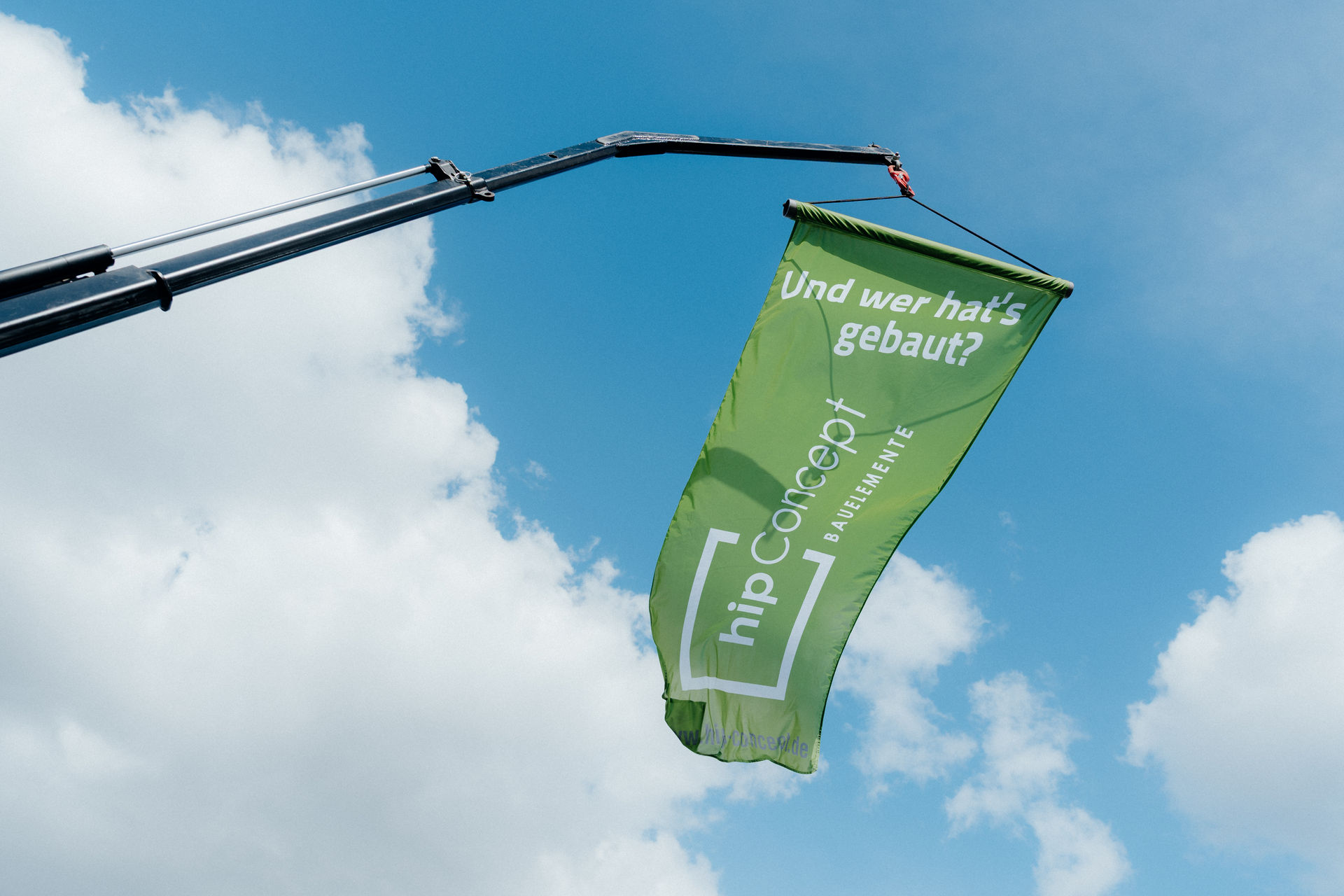 es weht eine Fahne im Wind, die an einem Kran aufgehängt wurde. Die Aufschrift ist "Und wer hat's gebaut?" Darunter ist das Logo von hip Concept zu sehen