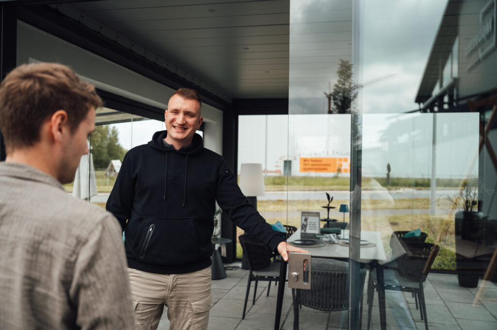 Ein Verkäufer im schwarzen Pullover zeigt eine Ganzglasschiebetür im Beratungssgespräch